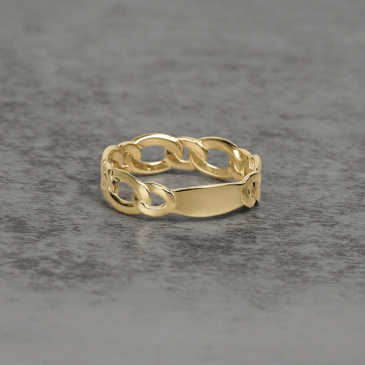 Detailed product view of a gold chain-link ring resting on a textured surface.