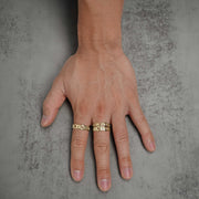 Hand wearing two solid gold Figaro chain-link rings on a neutral surface.