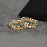 Two interlocking 10k and 14k gold classic Figaro band rings on textured surface.