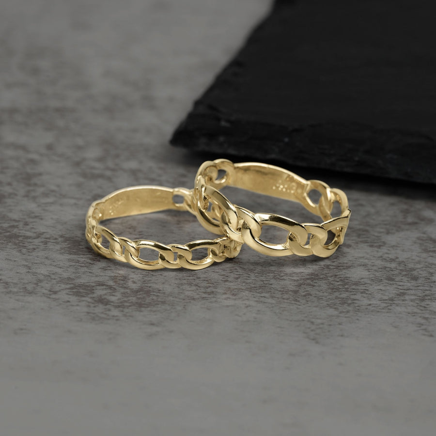Two interlocking 10k and 14k gold classic Figaro band rings on textured surface.
