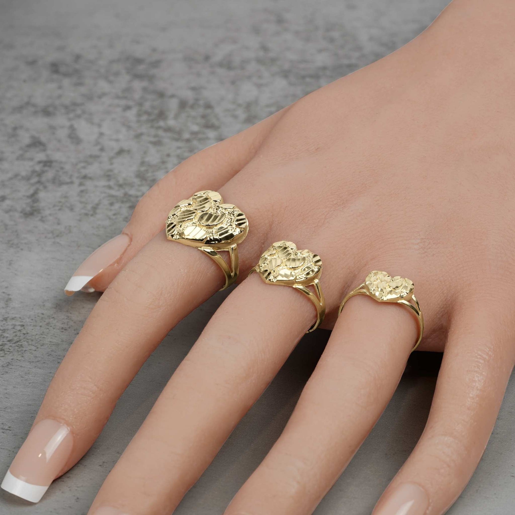 Three sizes of textured diamond-cut gold heart nugget rings styled beautifully on a hand.