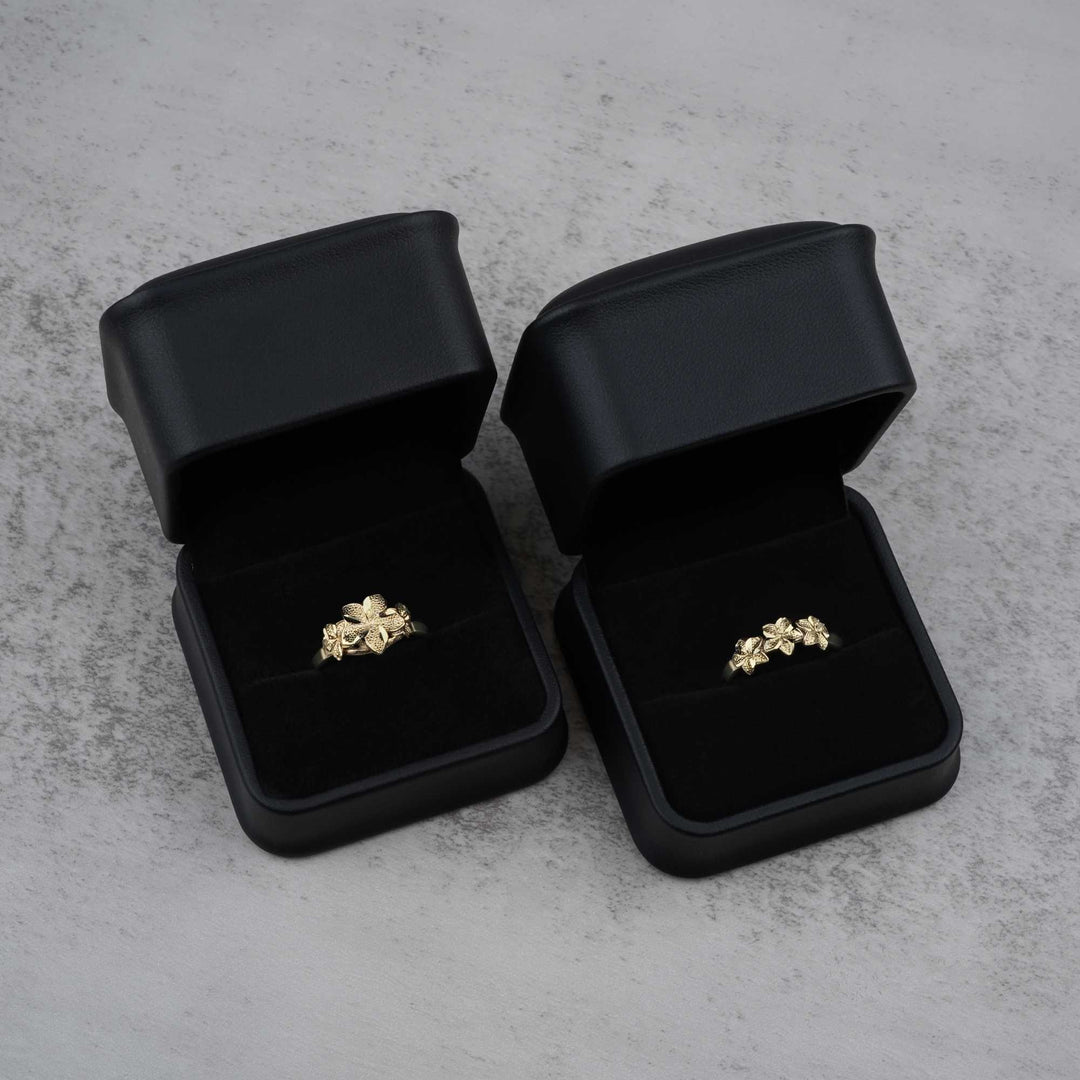 Two black jewelry boxes with 10k- 14k gold rings with floral design on a gray surface