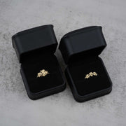 Two black jewelry boxes with 10k- 14k gold rings with floral design on a gray surface