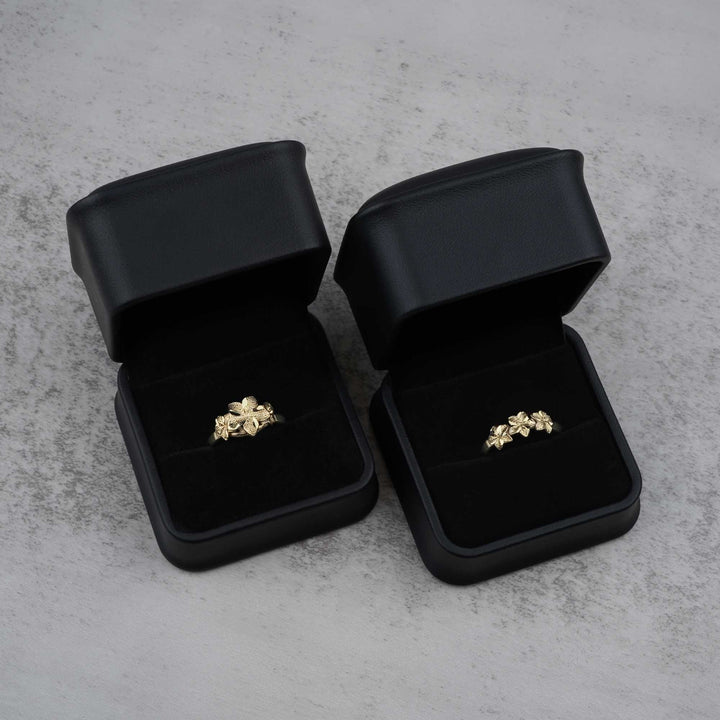 Two black jewelry boxes with 10k- 14k gold rings with floral design on a gray surface