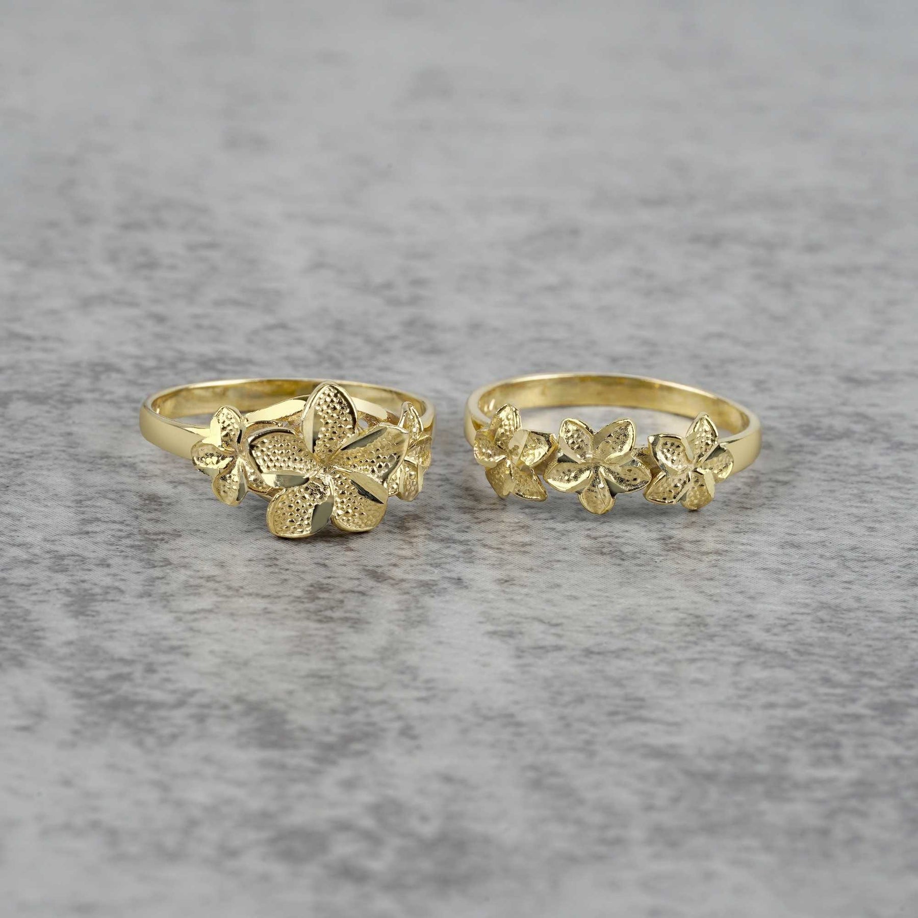 Two gold rings with floral designs on a gray background