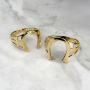 Two high-polish yellow gold horseshoe rings displayed on a white marble surface.