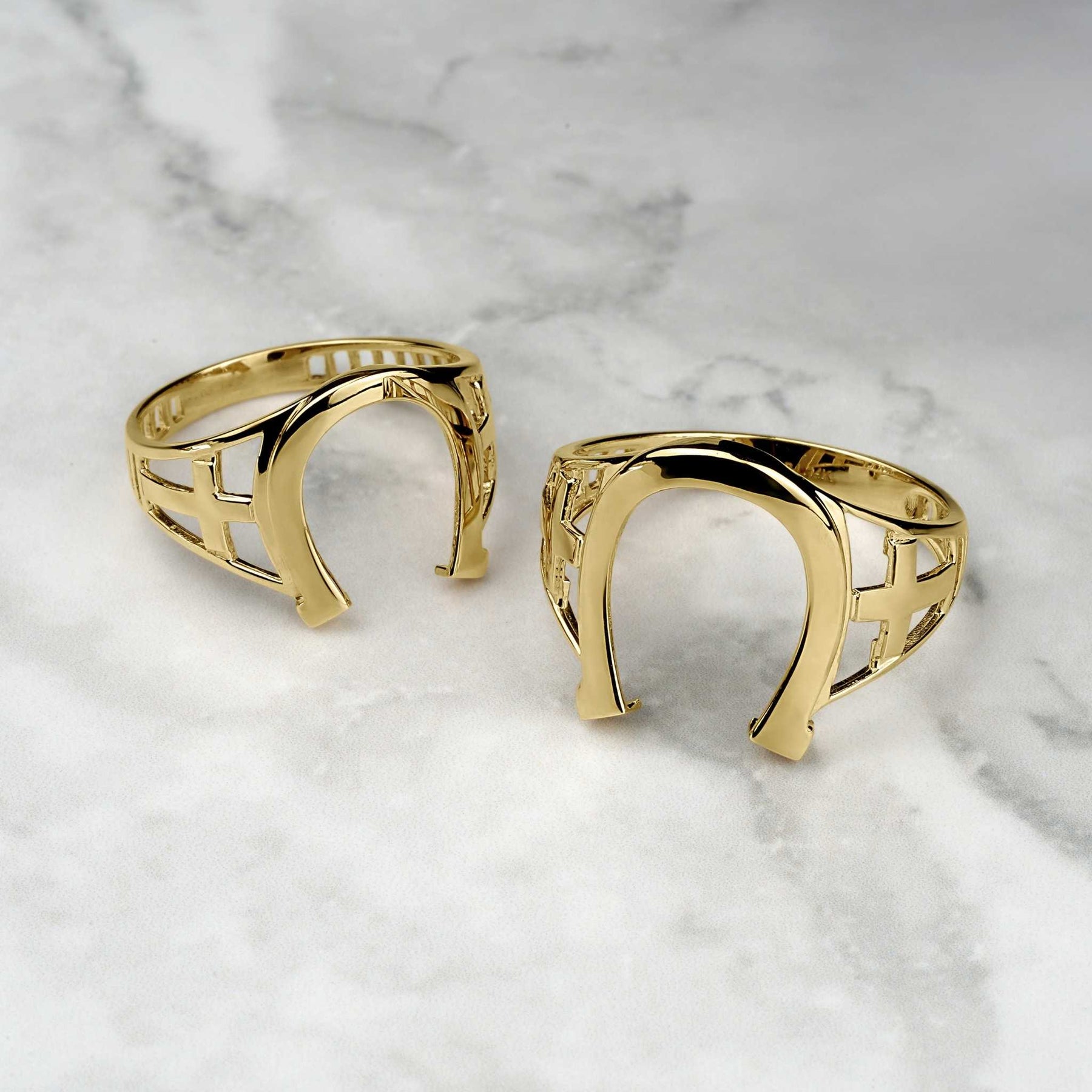 Two high-polish yellow gold horseshoe rings displayed on a white marble surface.