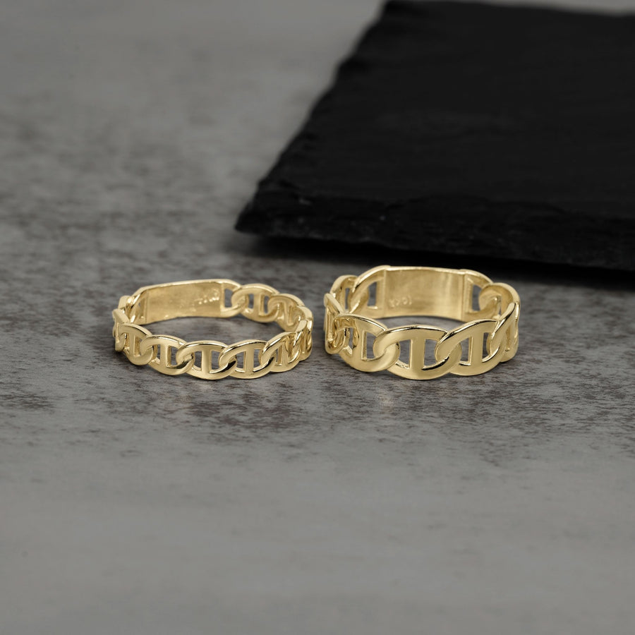 Two gold chain-link rings on a gray surface with a black cloth in the background.