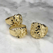 Three gold nugget oval rings displayed on a white marble background.