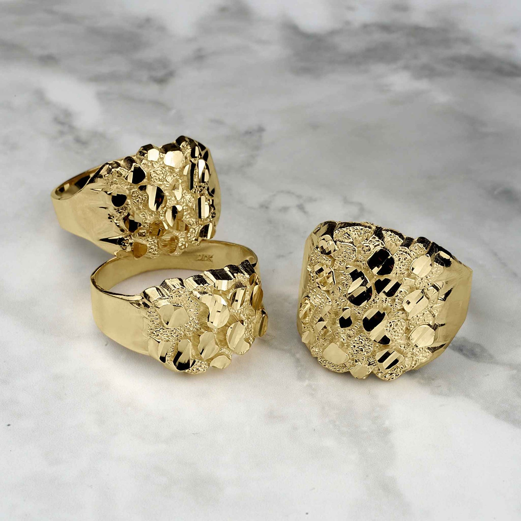 Three gold nugget oval rings displayed on a white marble background.