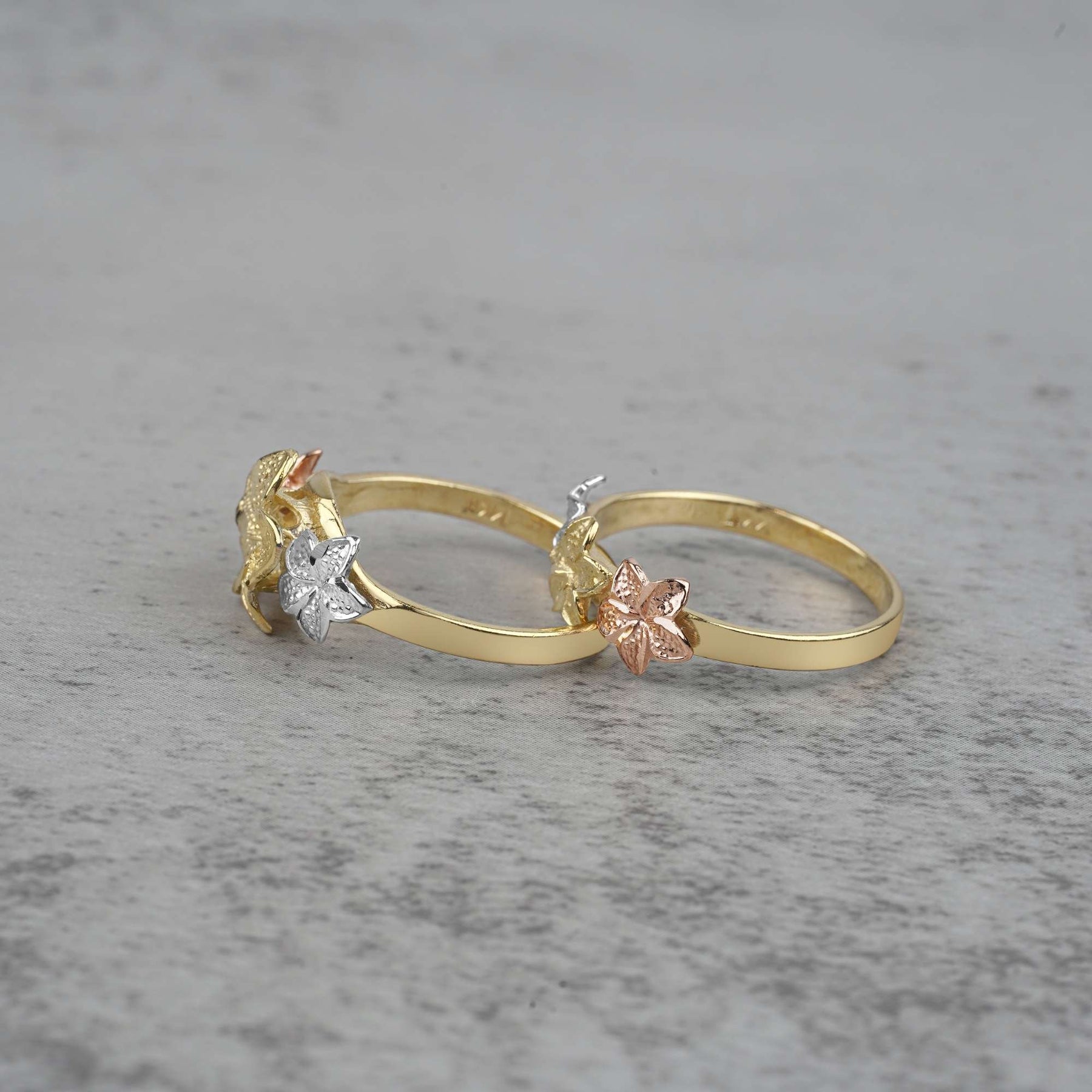 two 10k - 14k gold rings with floral designs on a gray surface