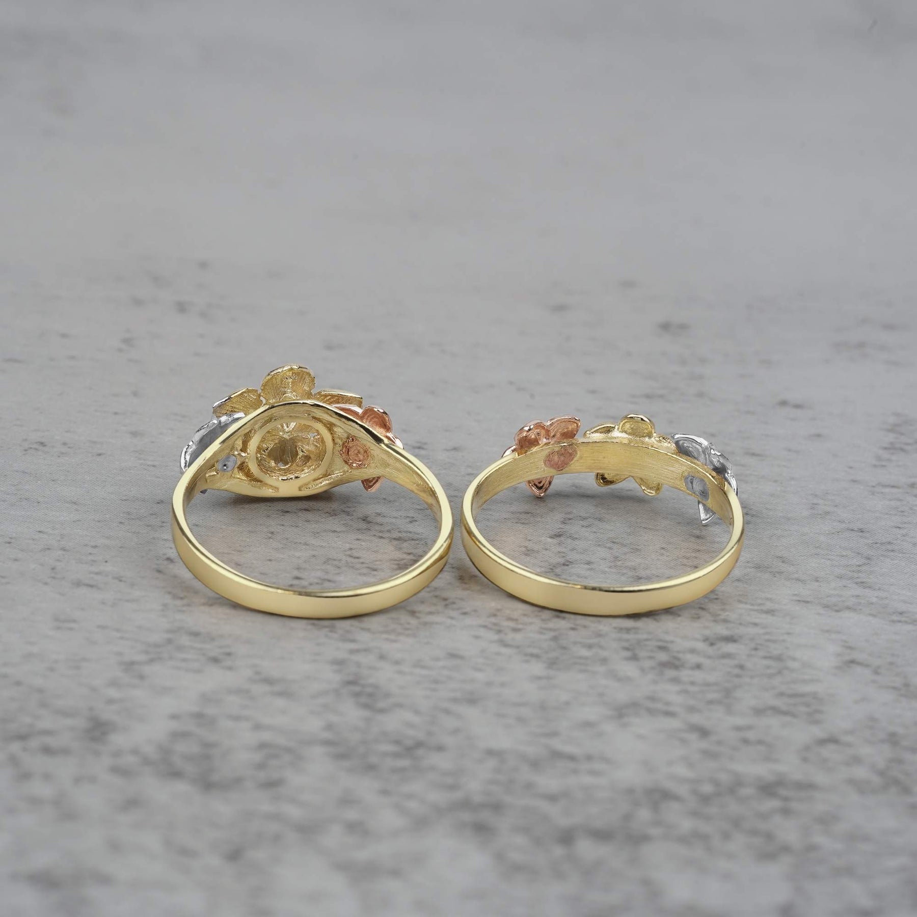 Two 10k - 14k gold rings with floral design back view on a gray surface