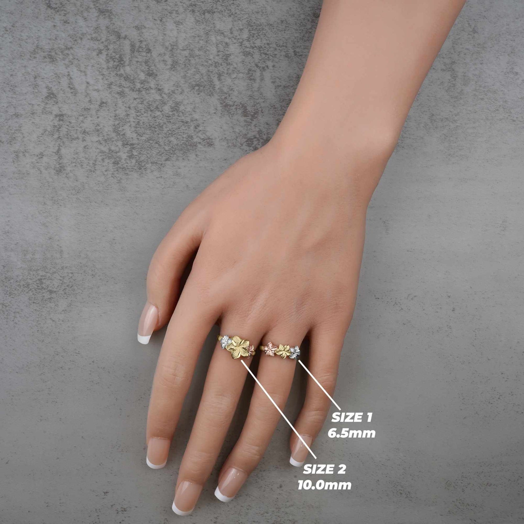 Hand wearing a two 10k - 14k gold ring with floral design on a gray concrete background