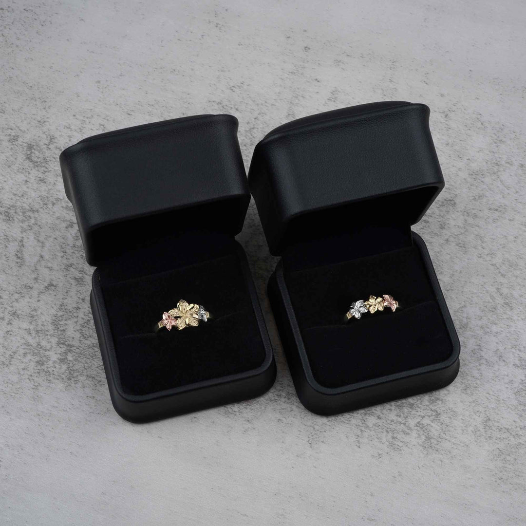 Two 10k - 14k gold rings with a floral design in black jewelry boxes on a gray surface