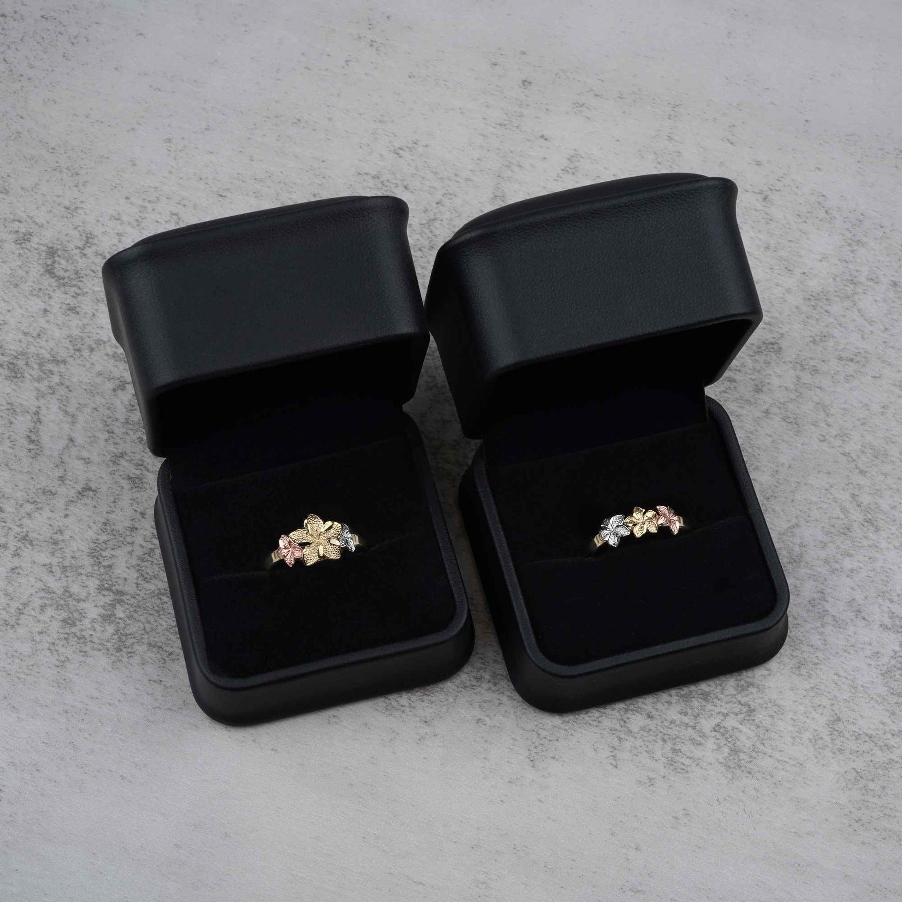 Two 10k - 14k gold rings with a floral design in black jewelry boxes on a gray surface