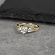 Three-stone gold ring with heart-shaped white cubic zirconia on gray background.