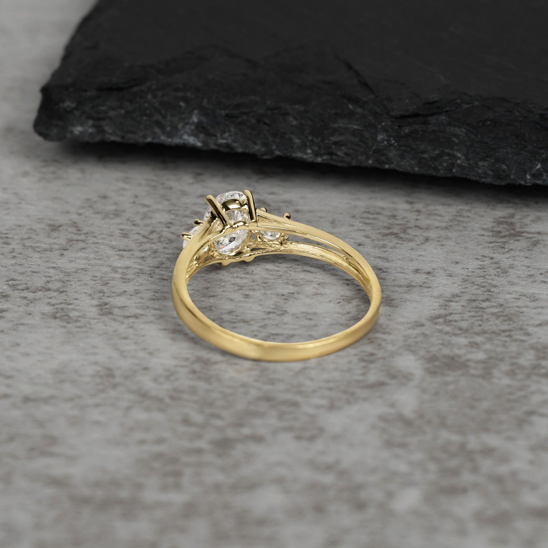 Back view of a gold three-stone ring with an oval center stone on gray stone.