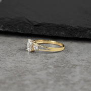 Three-stone gold ring with oval white cubic zirconia from a side view perspective.
