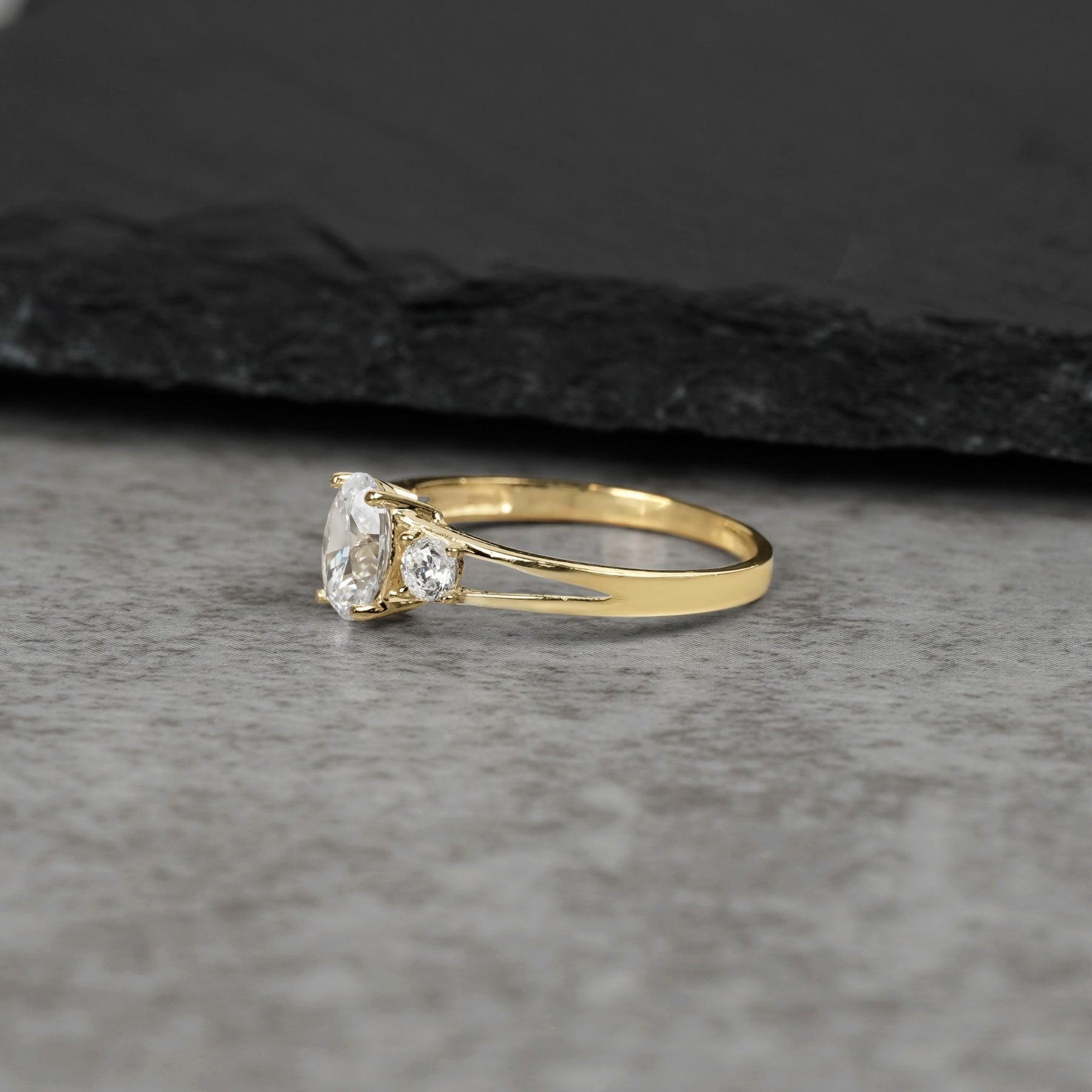Three-stone gold ring with oval white cubic zirconia from a side view perspective.