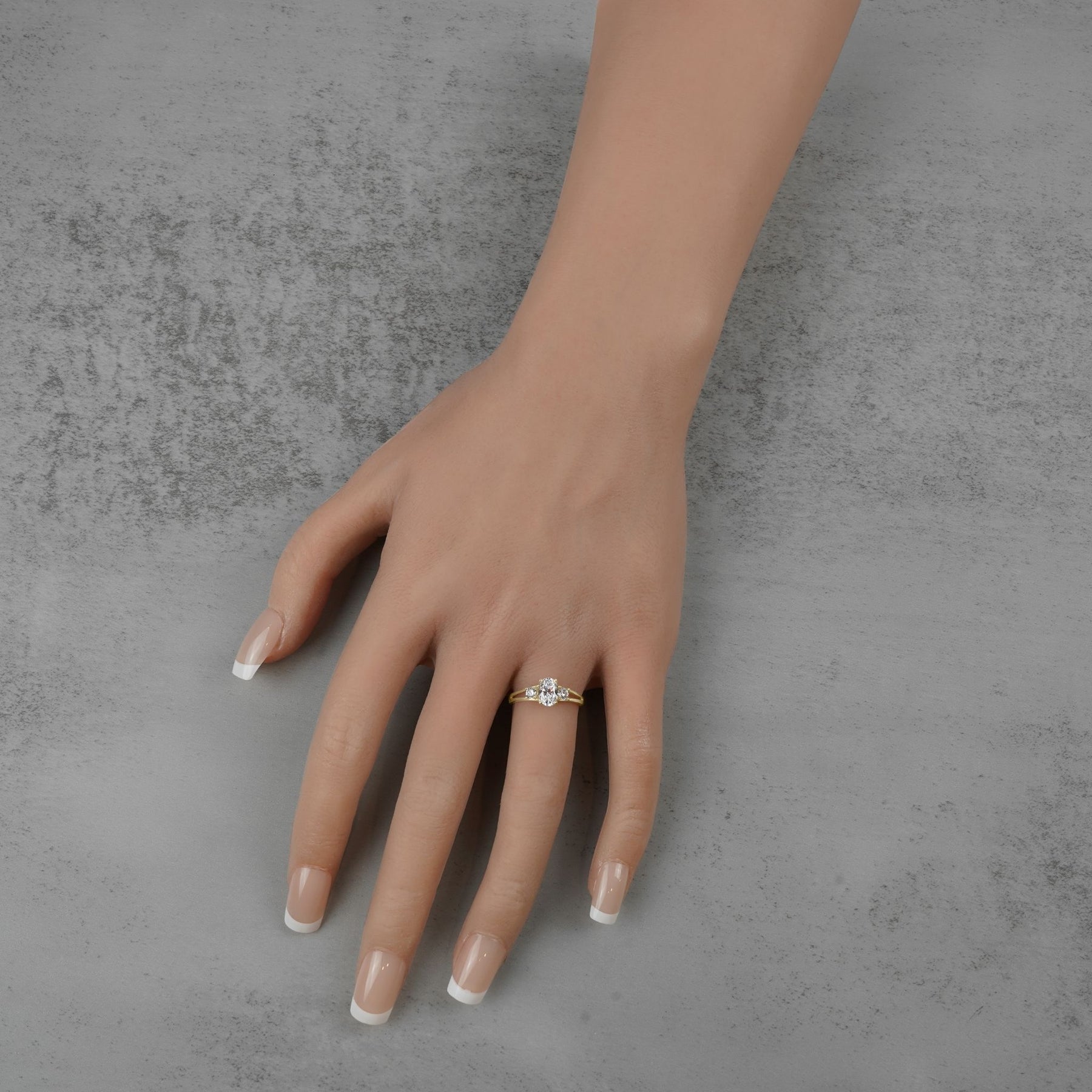 Gold three-stone ring with an oval center stone worn on a model's hand.