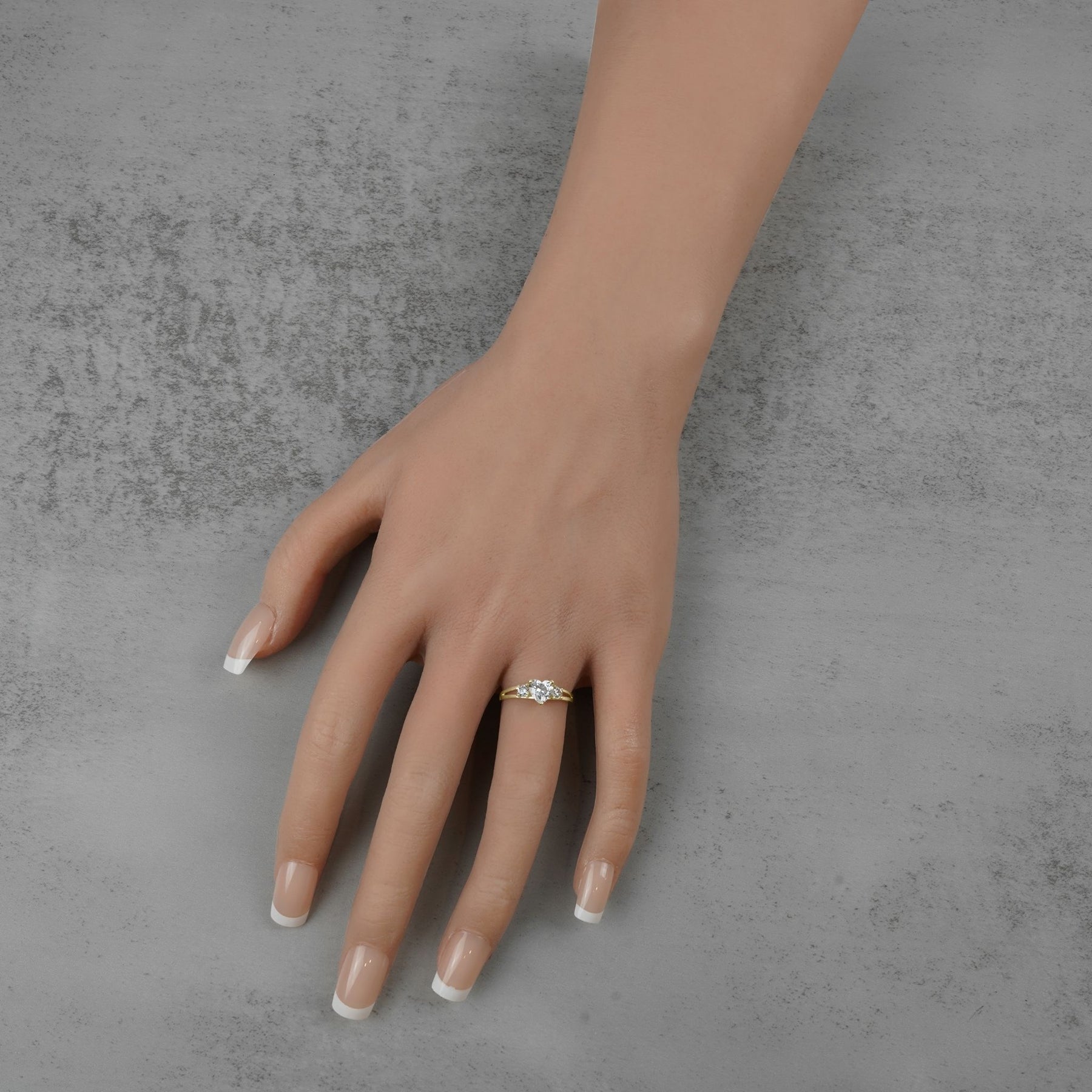 Gold three-stone ring with heart-shaped white cubic zirconia worn on a model's hand.