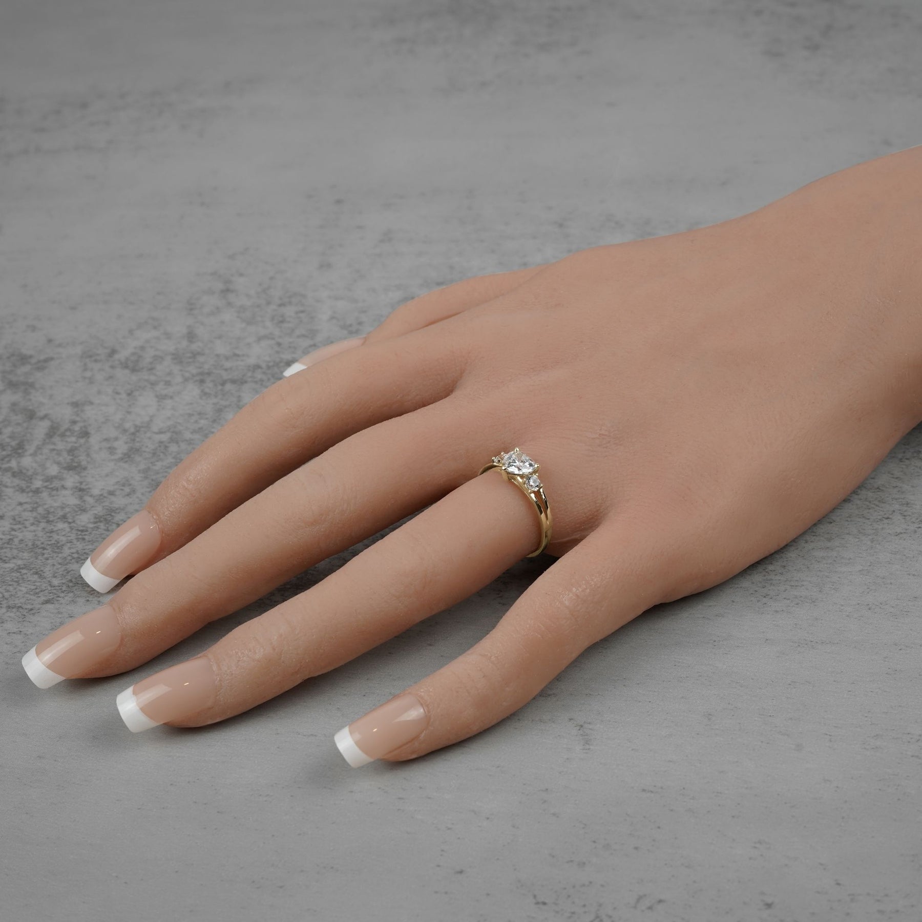 Side view of a gold three-stone ring with heart-shaped diamonds on a hand.