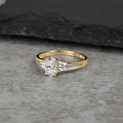 Three-stone gold ring with an oval cubic zirconia on a gray background.