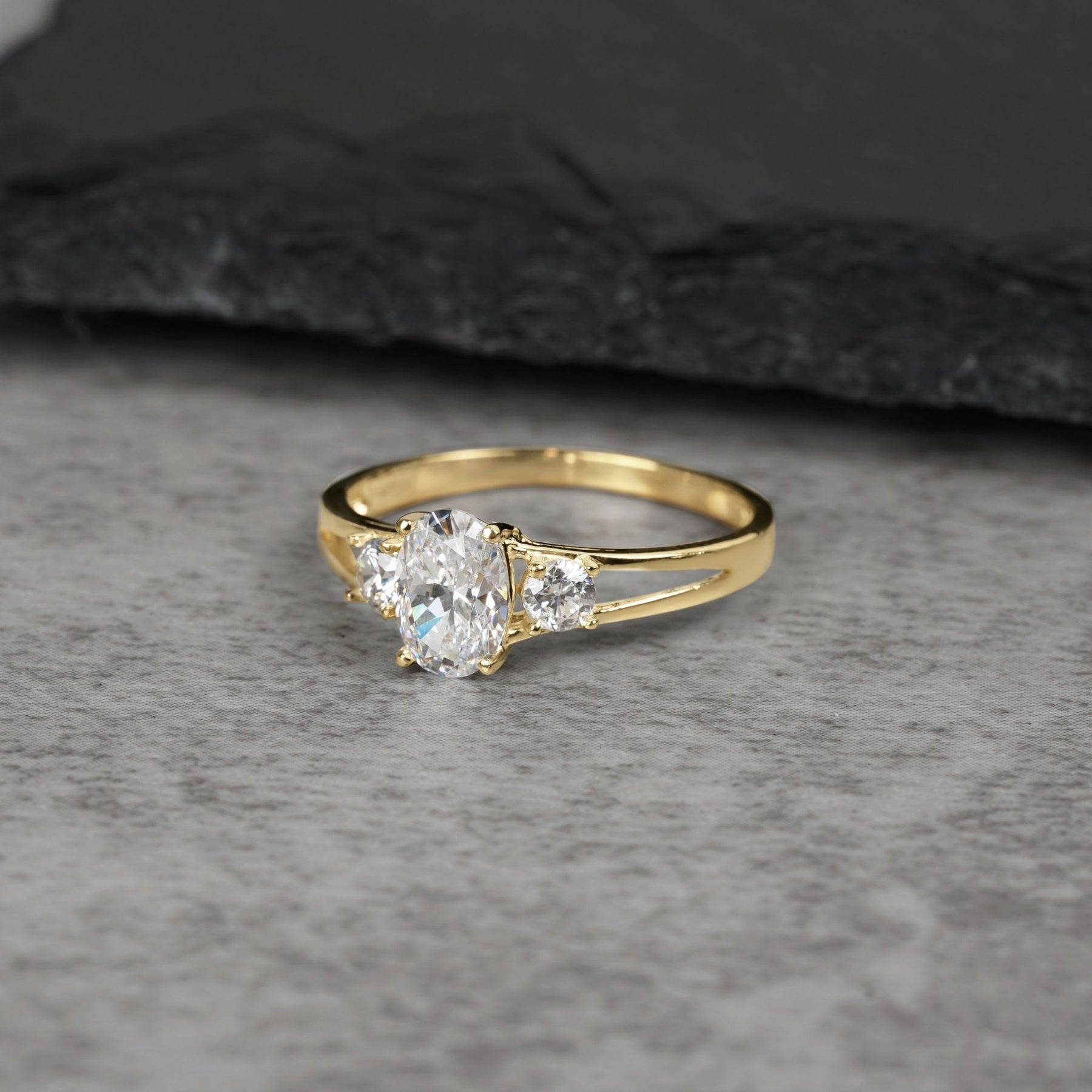 Three-stone gold ring with an oval cubic zirconia on a gray background.