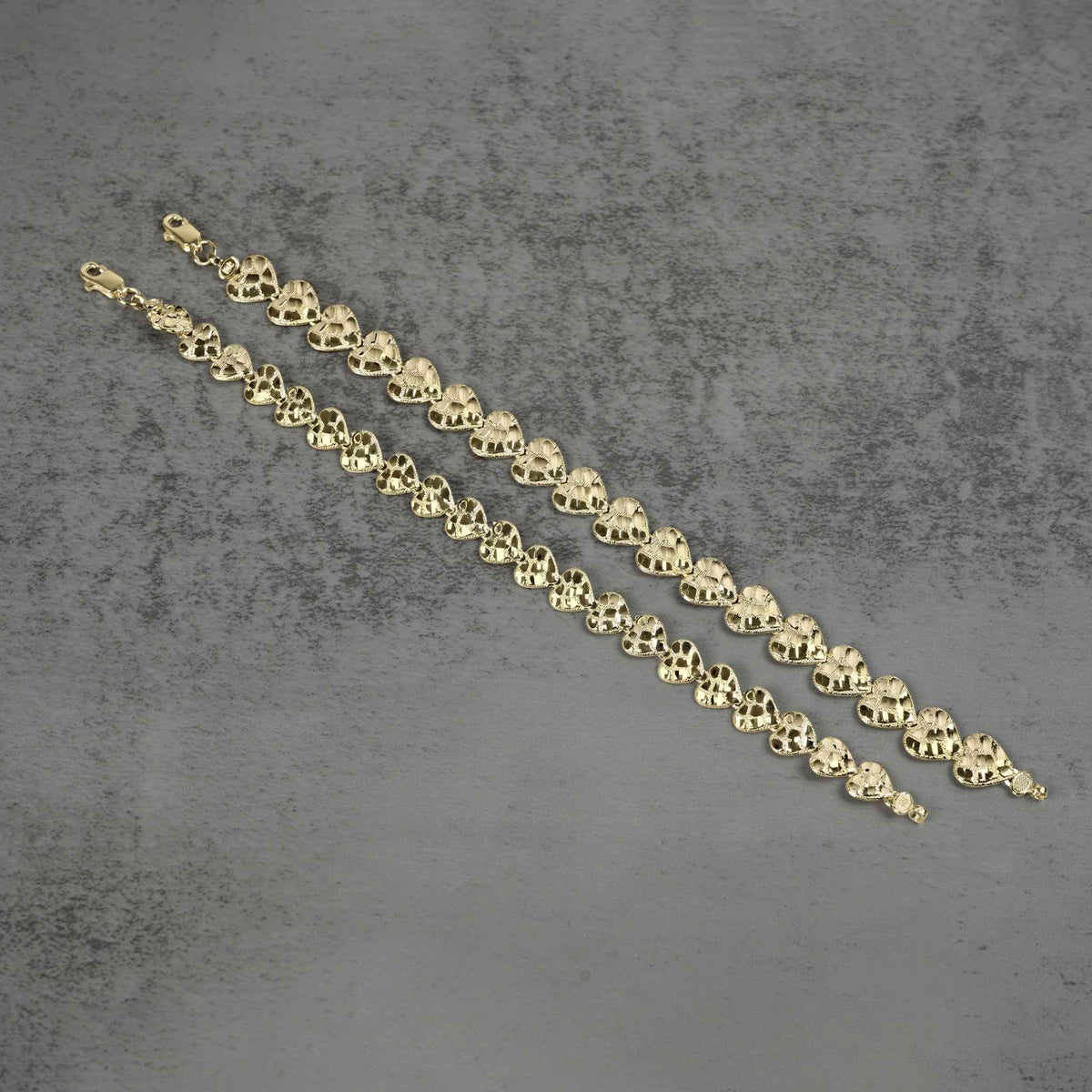 Two gold concave nugget heart link bracelets placed diagonally on a gray surface.