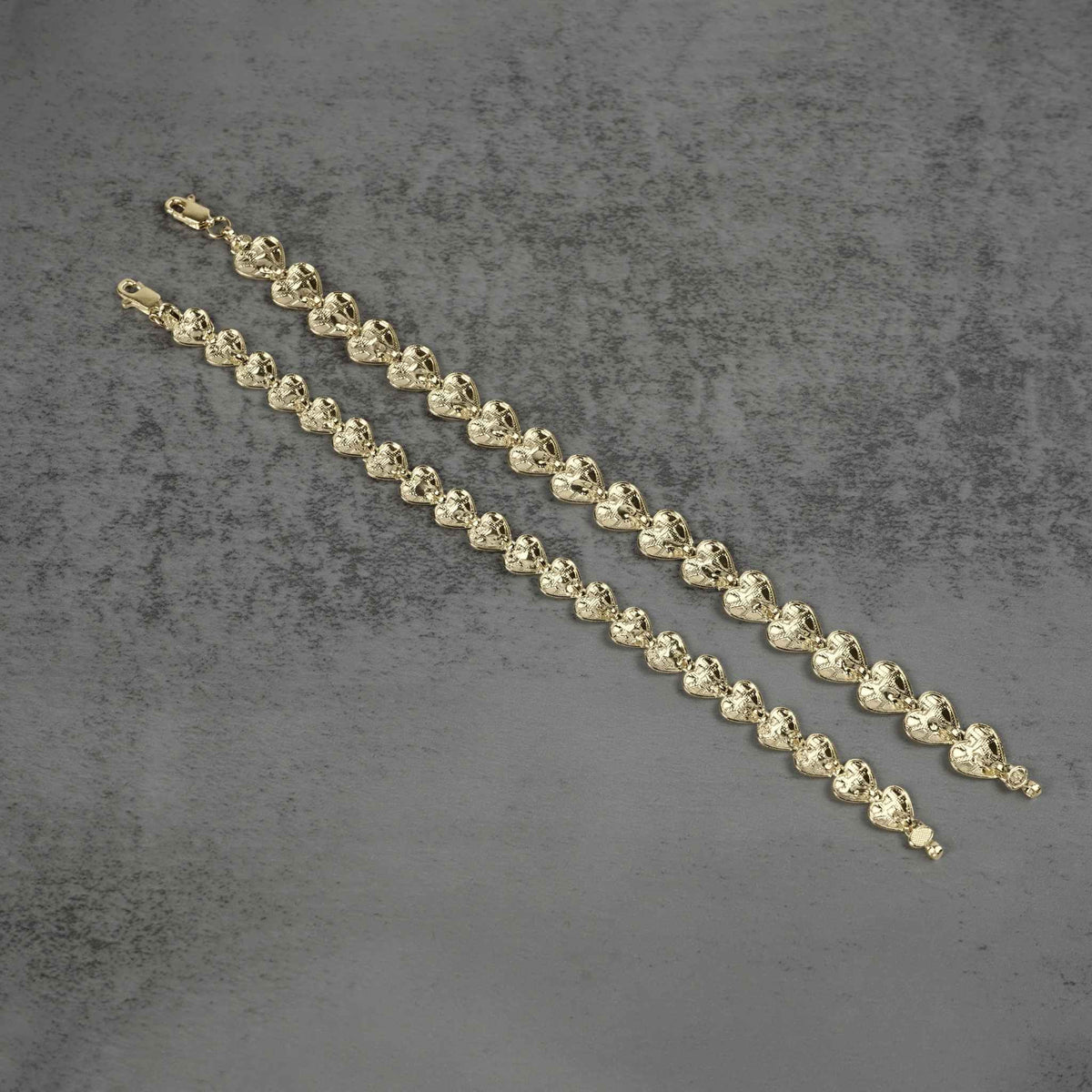Back view of two gold nugget heart link bracelets on a gray background.