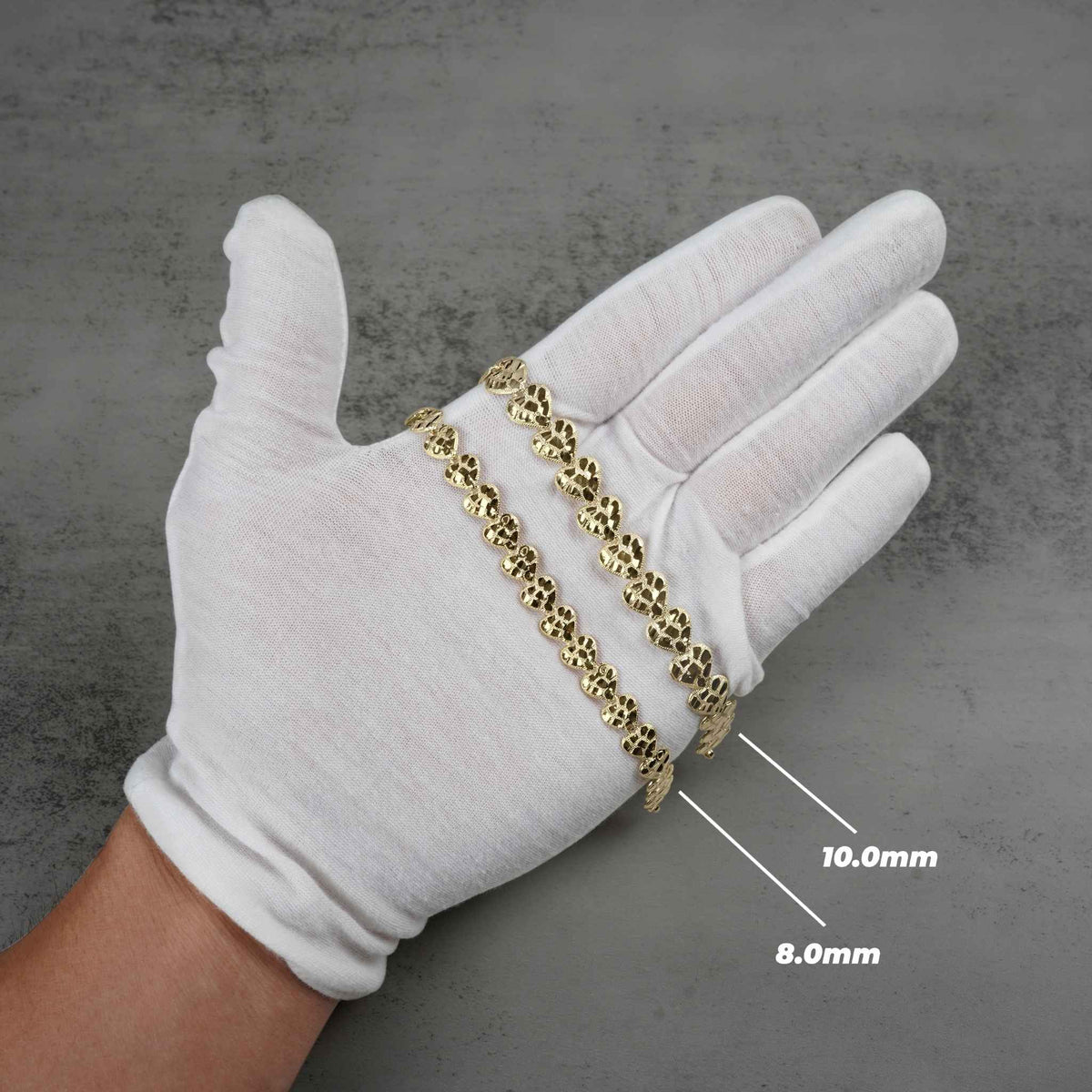 White gloved hand holding 8.0mm and 10.0mm gold nugget heart link bracelets.