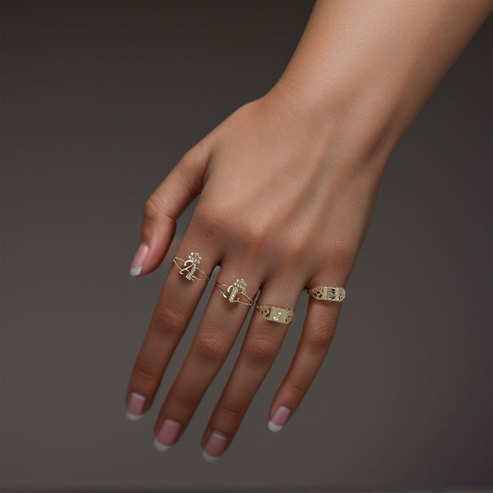 Model wearing multiple 10k gold crown cursive initial CZ rings against a dark background.