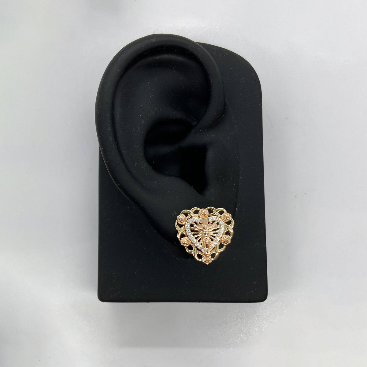 Two-tone gold crucifix and rose heart stud earring displayed on a black ear stand.