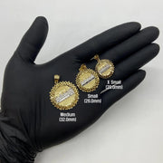 Gloved hand holding three sizes of round gold Last Supper pendants labeled Medium, Small, and X Small.