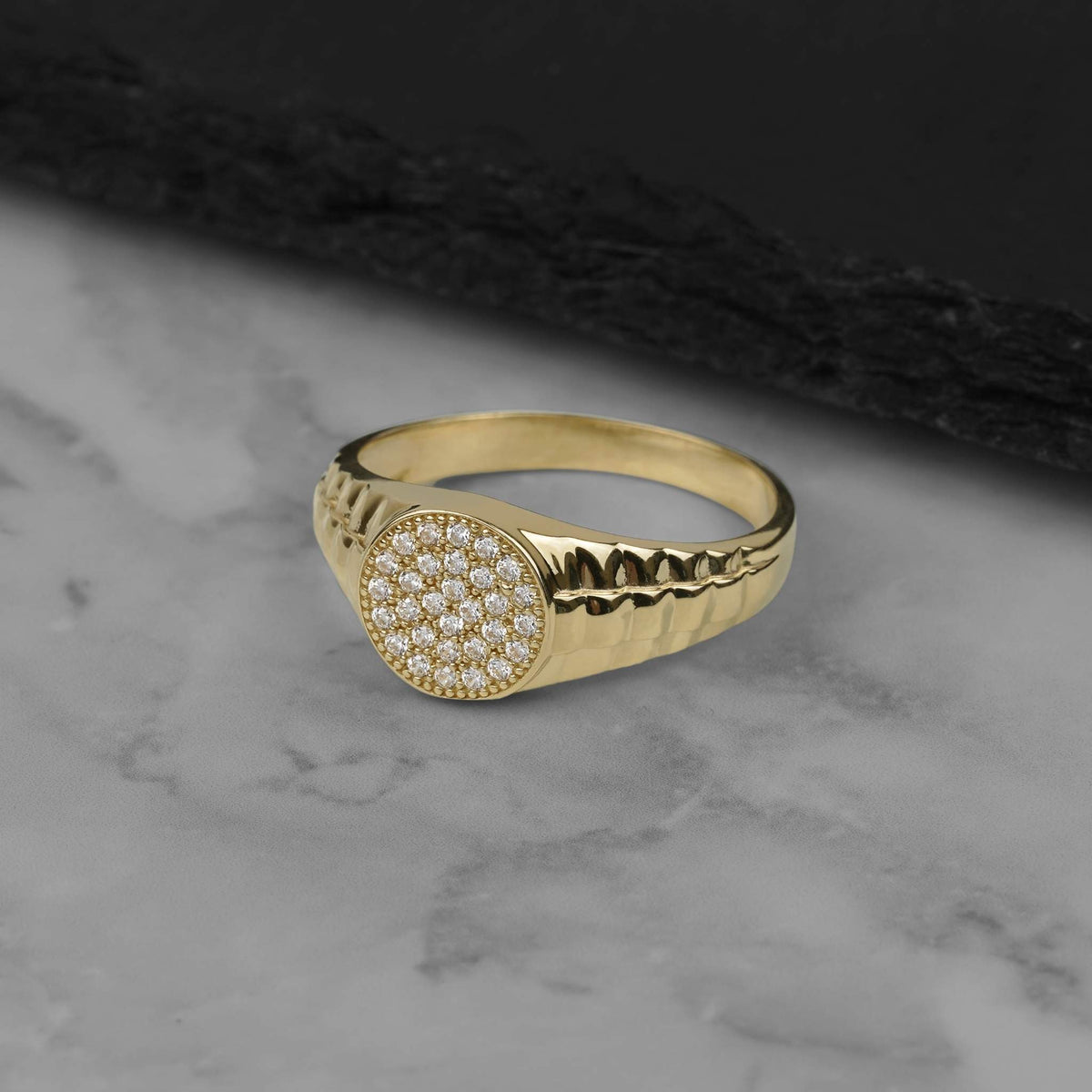 10k 14k yellow gold signet ring with a round face set with clear cubic zirconia stones and a textured band, shown at an angle.