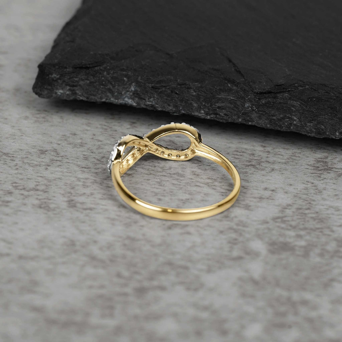 Profile view of the 10k or 14k gold Elio infinity ring on stone surface.