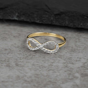 Yellow gold infinity ring paved with cubic zirconia resting on a grey textured stone surface.