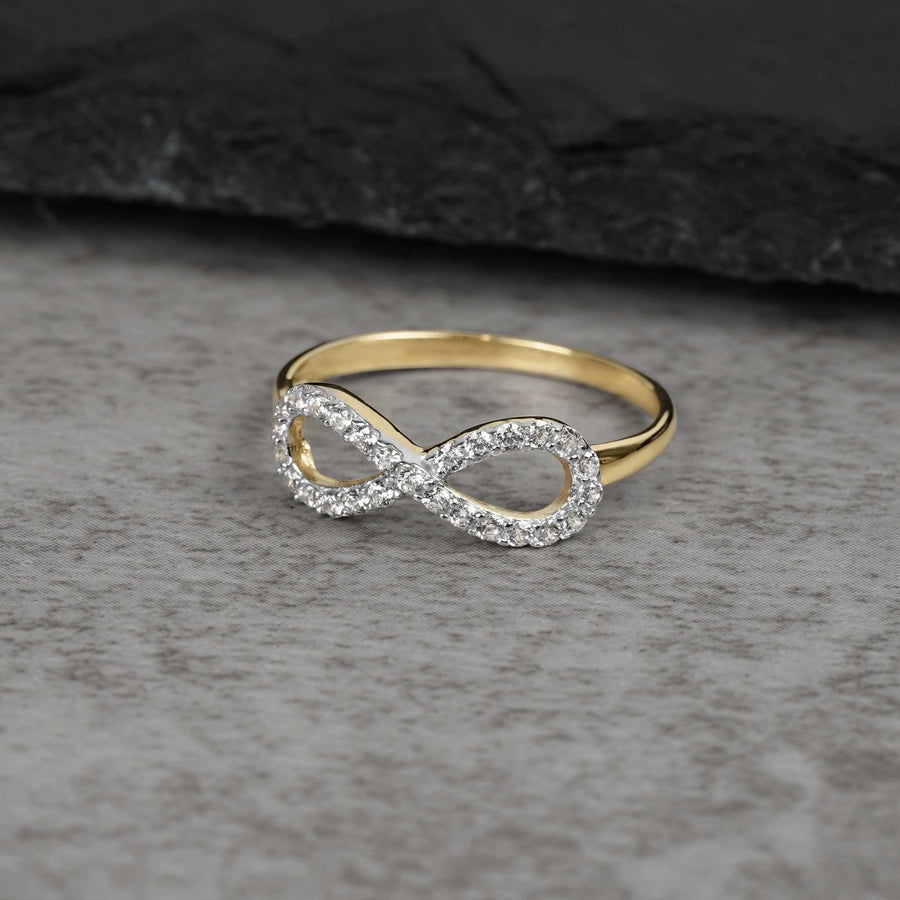 Yellow gold infinity ring paved with cubic zirconia resting on a grey textured stone surface.