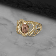 A 10k and 14k gold Elyra heart Virgin Mary ring on a marble surface.