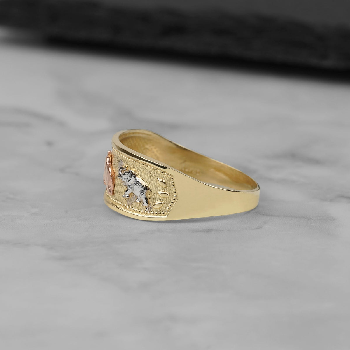 Side view of the tricolor gold Evora lucky elephant ring on marble.