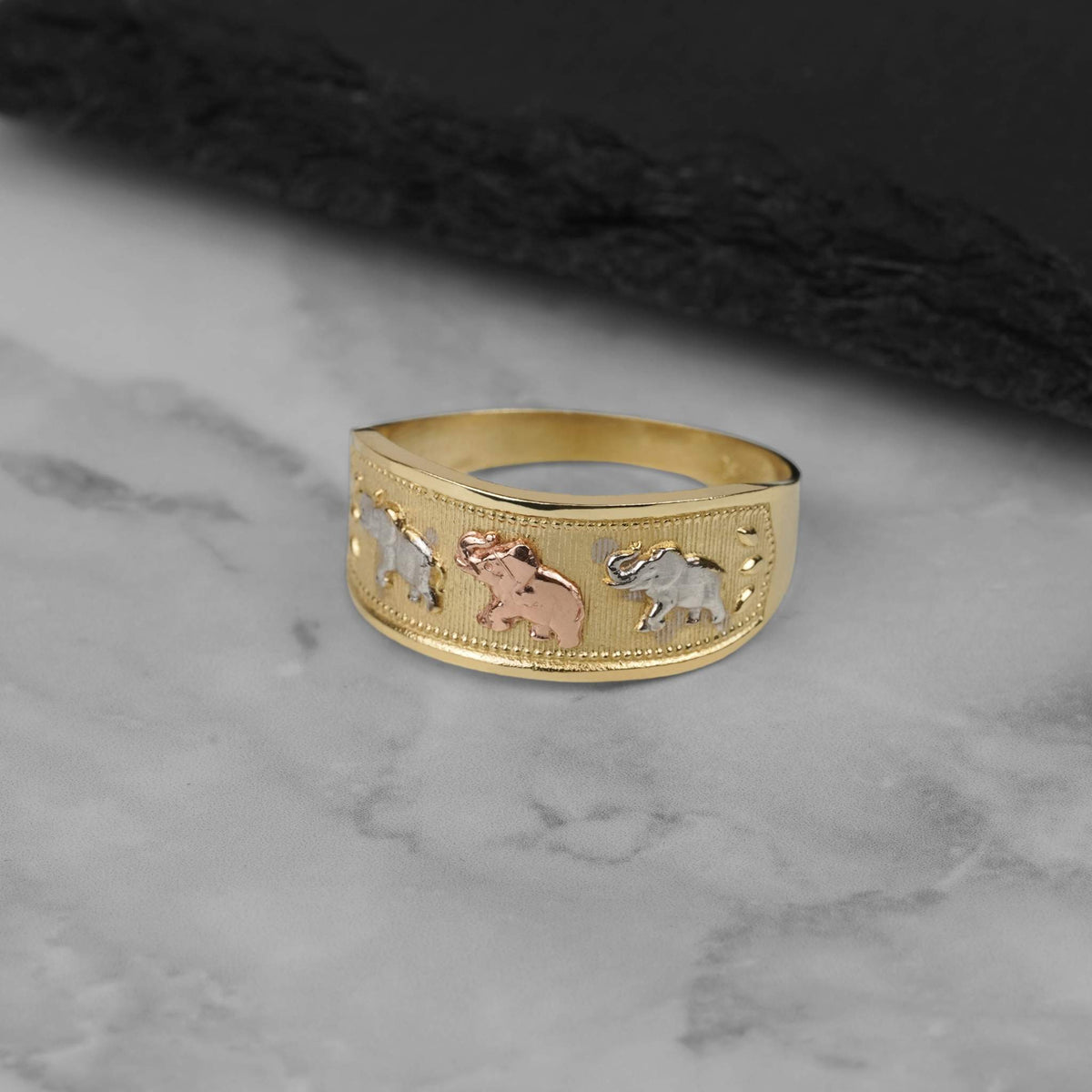Tri-color gold Evora lucky elephant ring resting on a marble countertop surface.