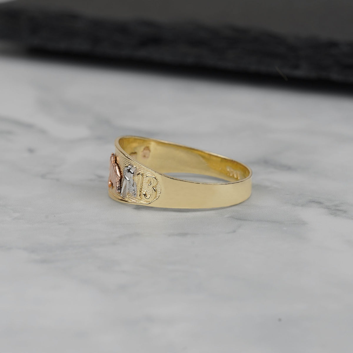 Side view of the tricolor gold ring resting on a white marble surface.