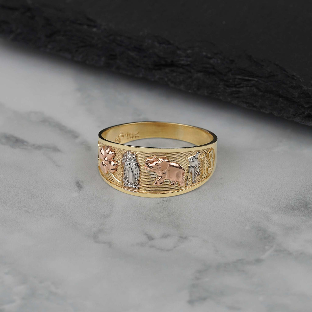 Tri-color gold band featuring various lucky charm motifs on a dark textured surface