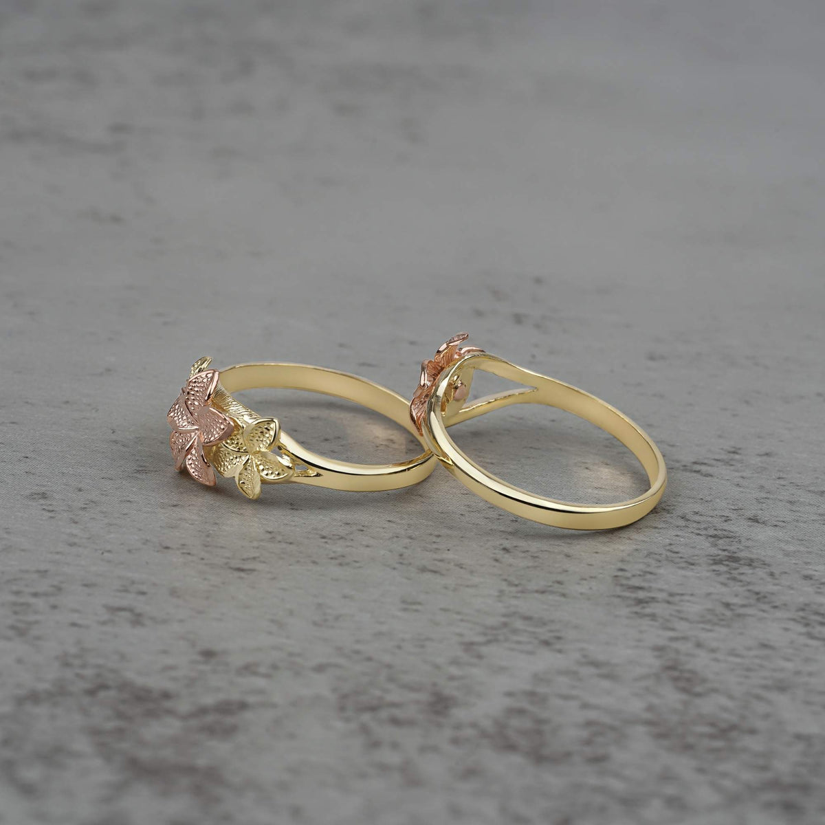 Two 10k - 14k gold rings with floral designs side view on a gray surface