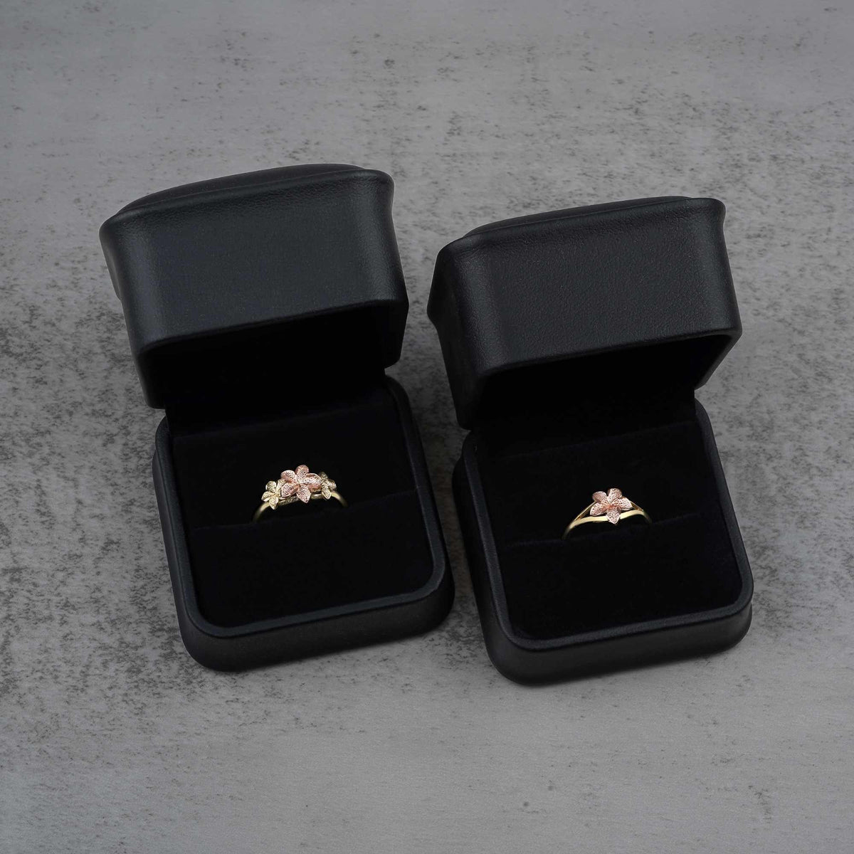 Two black jewelry boxes with two 10k - 14k gold rings with floral design