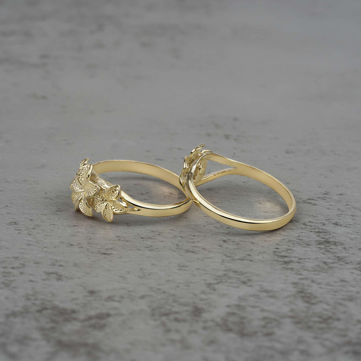 Two 10k - 14k gold rings with floral designs side view on a gray surface