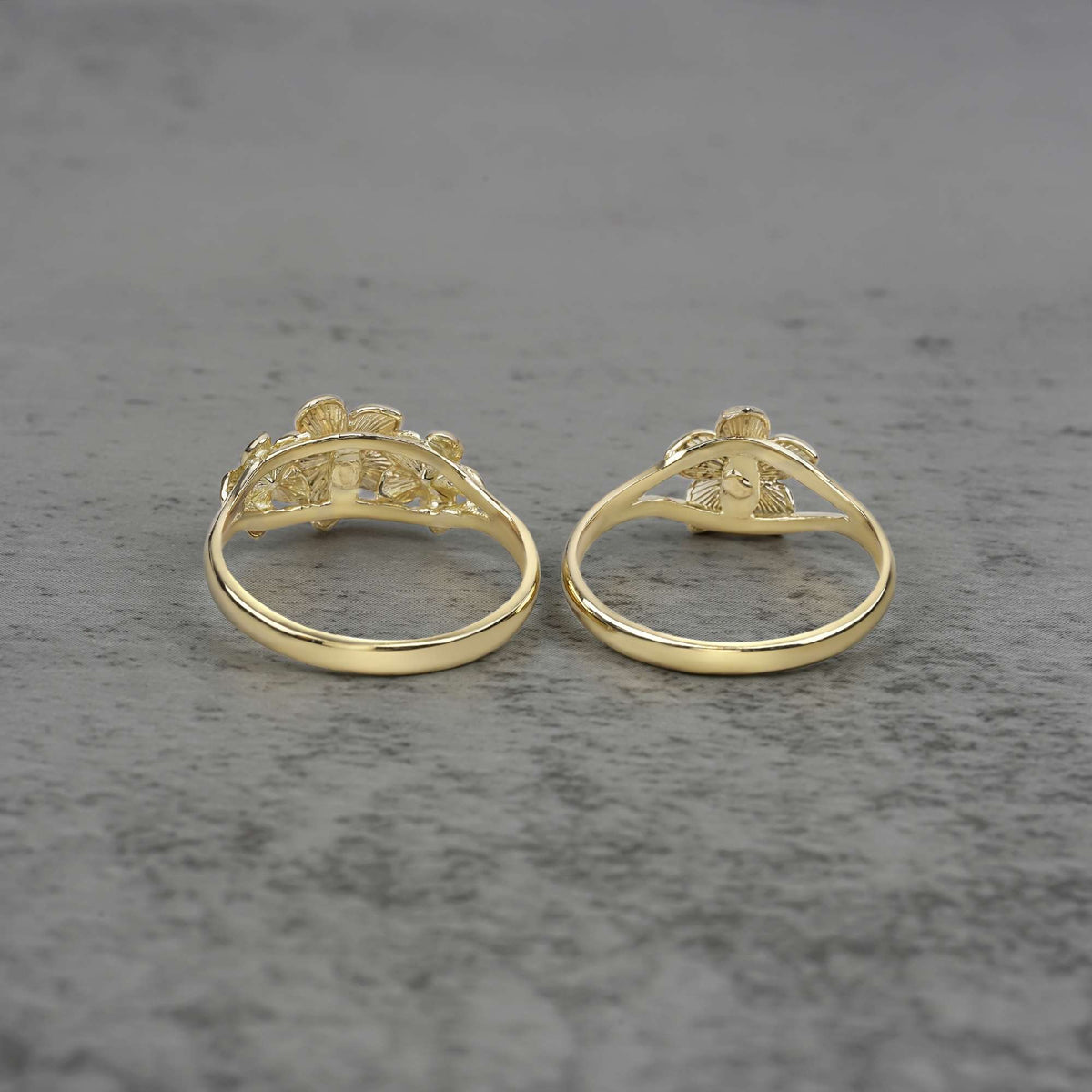 Two 10k - 14k gold rings with a floral design back view on a gray surface