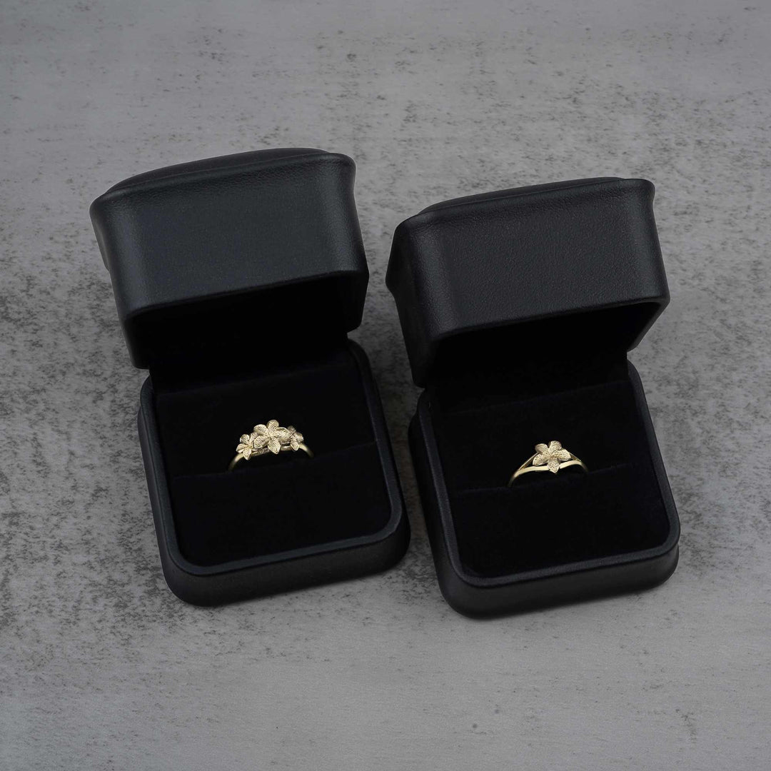 Two black jewelry boxes with two 10k - 14k gold rings with floral design 
