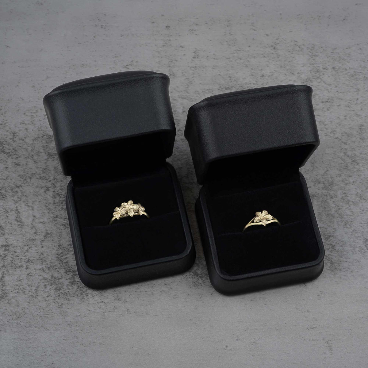 Two black jewelry boxes with two 10k - 14k gold rings with floral design 
