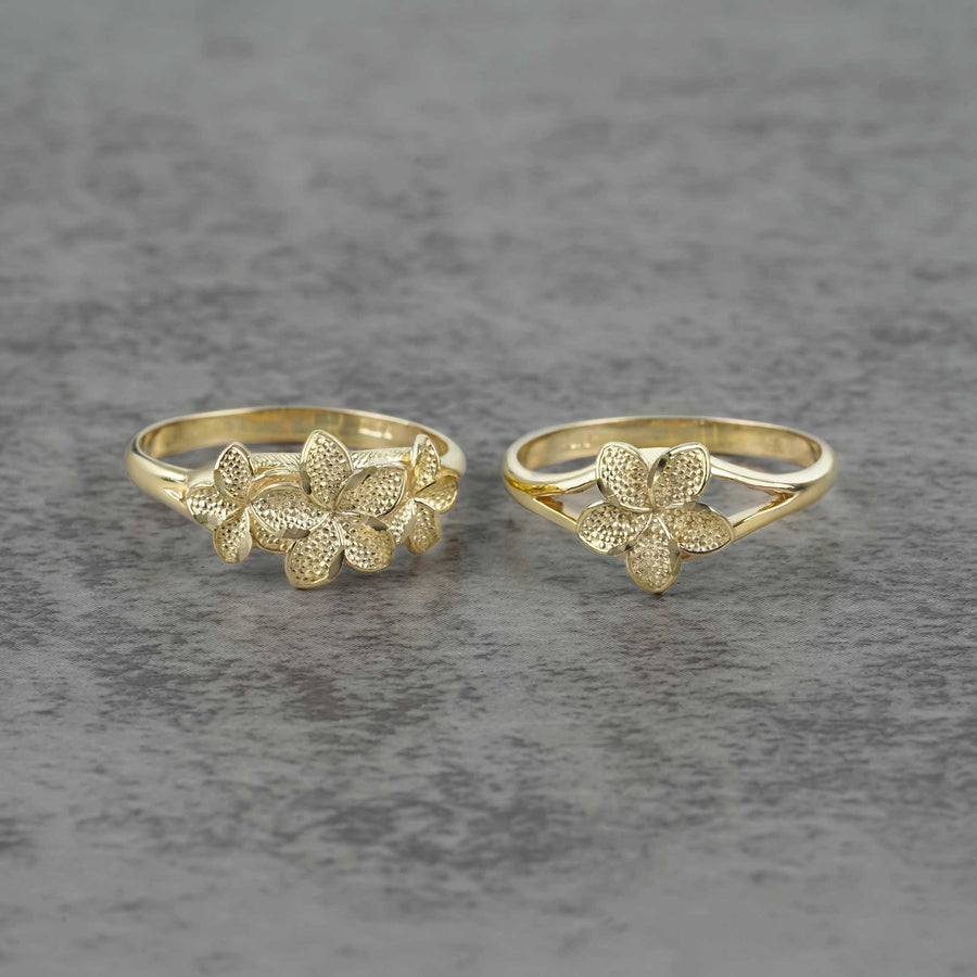 Two 10k - 14k gold rings with floral designs on a gray surface